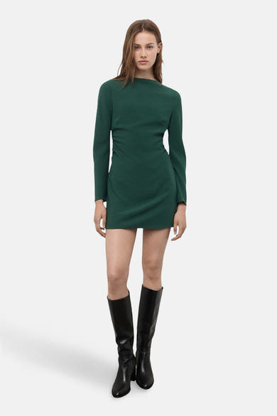 Robe verte à manches longues de MANGO, avec des plis décoratifs et des bottes hautes noires.
