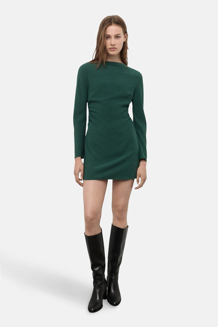 Robe verte à manches longues de MANGO, avec des plis décoratifs et des bottes hautes noires.
