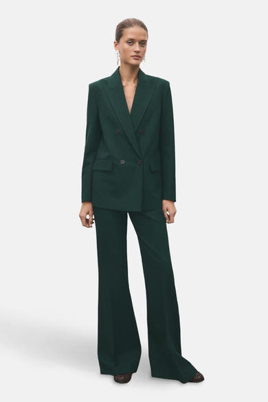 Pantalon vert de MANGO, coupe évasée et élégante, porté avec un tailleur coordonné et des boucles d'oreilles pendantes.