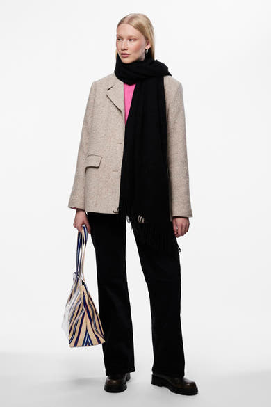 Zwarte sjaal van PIECES®, met franjes, gedragen met een beige blazer, een zwarte broek en een gestreepte tas.