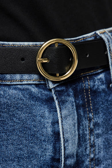 Zwarte PIECES® riem met gouden gesp, gedragen met een lichtblauwe jeans en een zwart T-shirt.