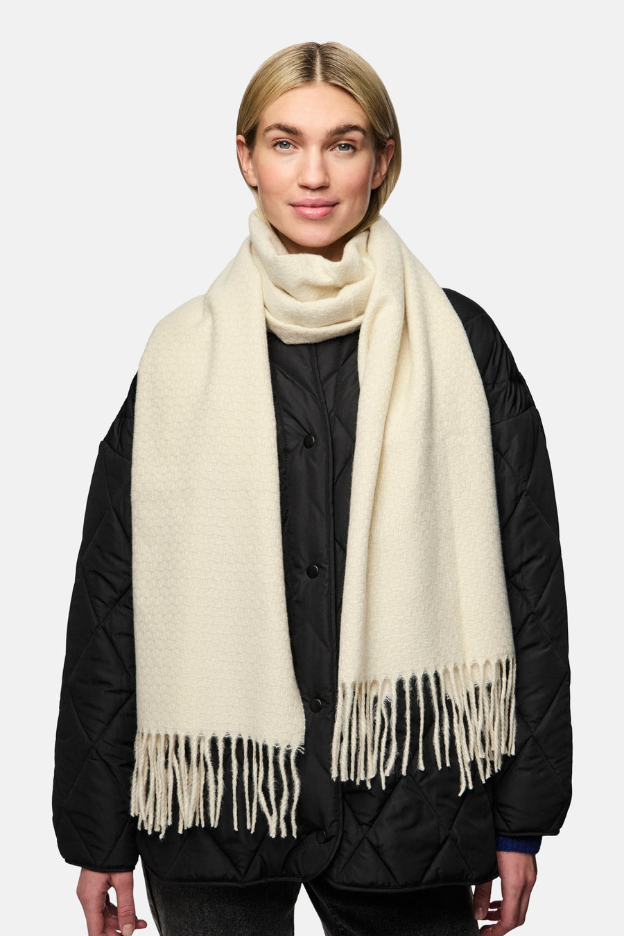 Écharpe blanche de PIECES, à franges, portée avec une veste matelassée noire.