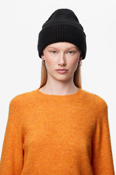 Bonnet noir de PIECES porté avec un pull orange et des boucles d'oreilles argentées.