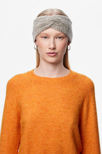 Beige oorwarmers van PIECES®, gedragen met ronde oorbellen en een oranje trui met textuur.