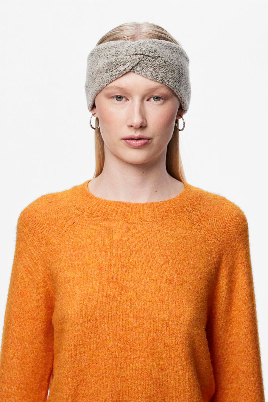 Beige oorwarmers van PIECES®, gedragen met ronde oorbellen en een oranje trui met textuur.