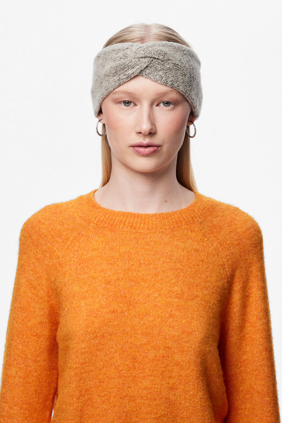 Beige oorwarmers van PIECES®, met een gebreide textuur, gedragen met een oranje trui en zilveren oorbellen.