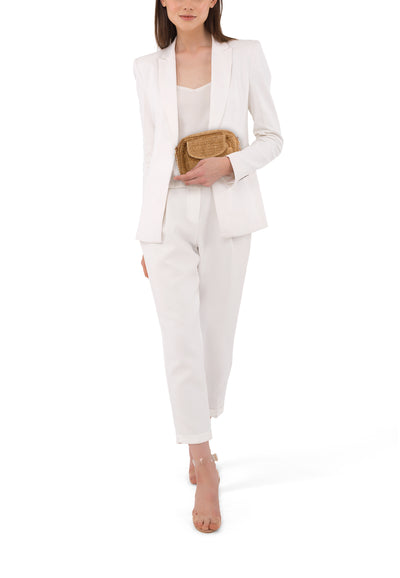 Sac à bandoulière brun tressé par PIECES®, porté avec un tailleur blanc et des sandales transparentes.
