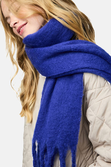 Écharpe bleu en maille, de PIECES®, portée avec une veste matelassée beige et les cheveux blonds ondulés.
