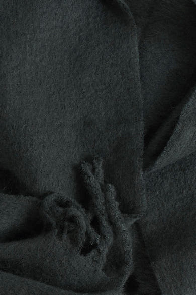 Écharpe verte en maille du PIECES®, texture floue et détail de franges nouées.
