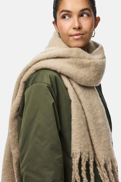 Beige sjaal van PIECES®, met een olijfgroene jas en ronde oorbellen.