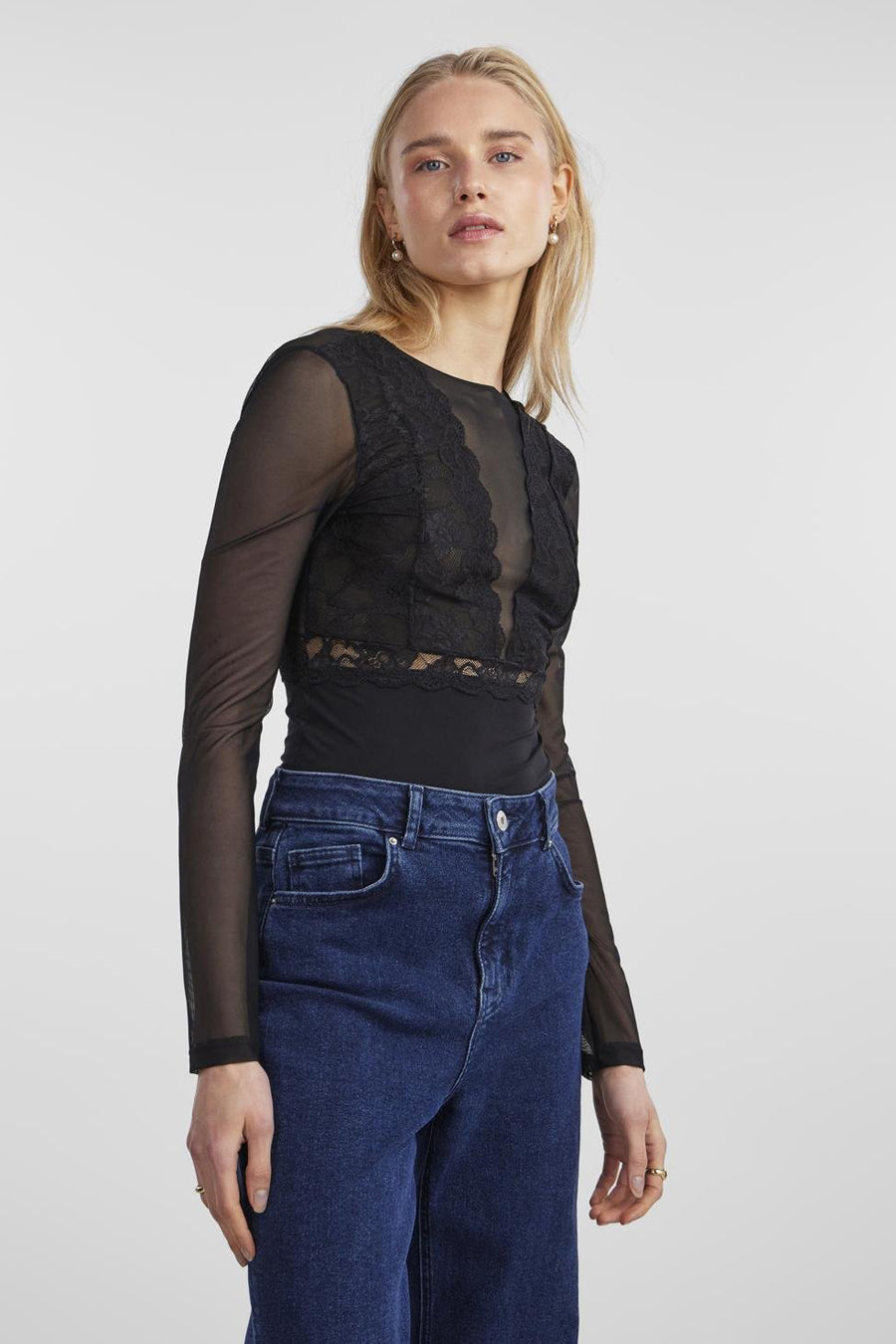 Body noir en dentelle par PIECES®, manches longues transparentes, porté avec un jean taille haute bleu foncé.
