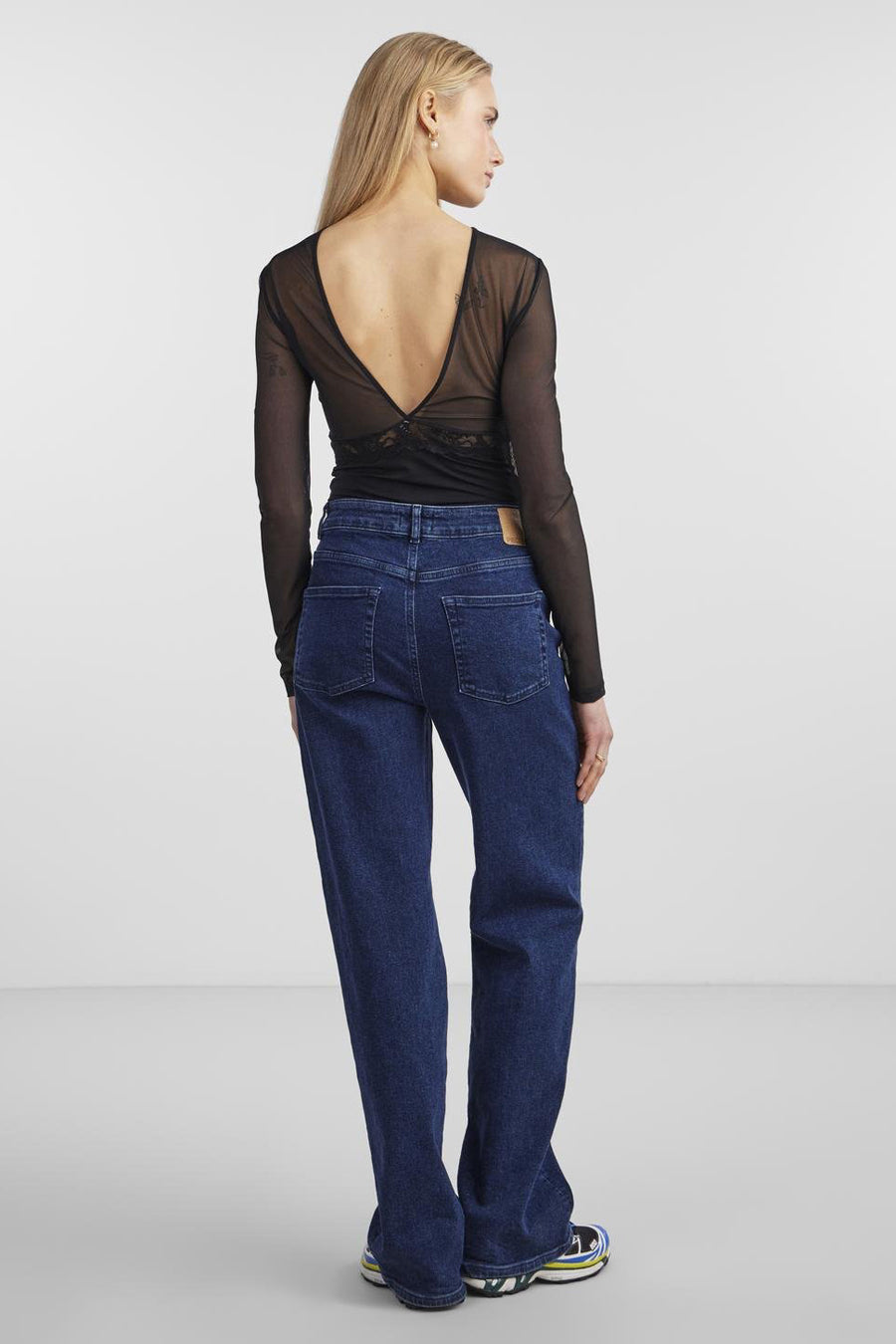 Body noir en dentelle par PIECES®, avec dos échancré et manches longues, porté avec un jean taille haute.
