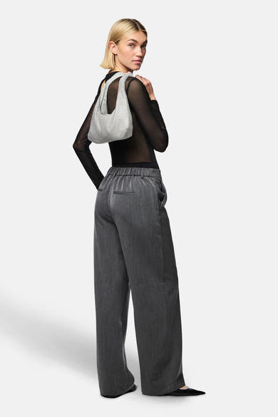 Body noir de PIECES®, porté avec un pantalon gris ample et un sac à main argenté.
