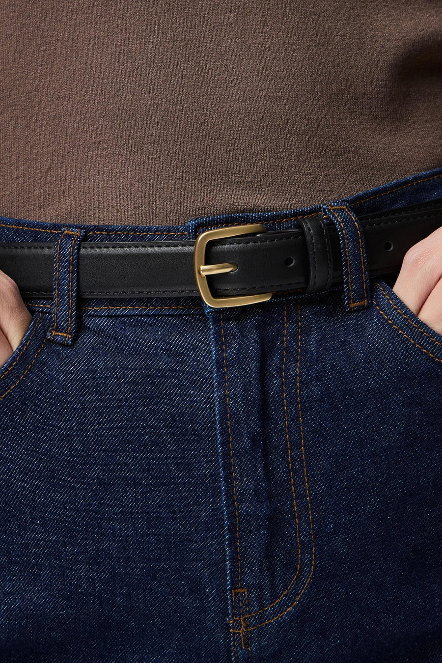Zwarte leren riem - PIECES®, met gouden gesp, gedragen met een donkere spijkerbroek en een bruine trui.