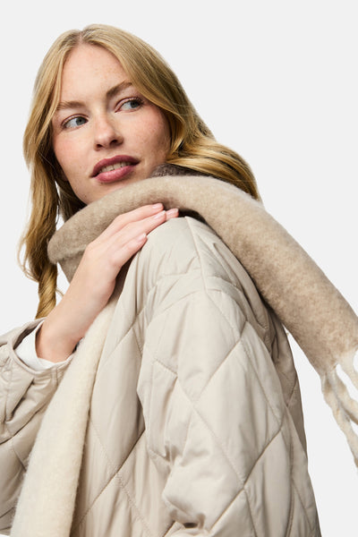 Écharpe beige de PIECES® avec des franges, portée avec un manteau matelassé couleur crème.
