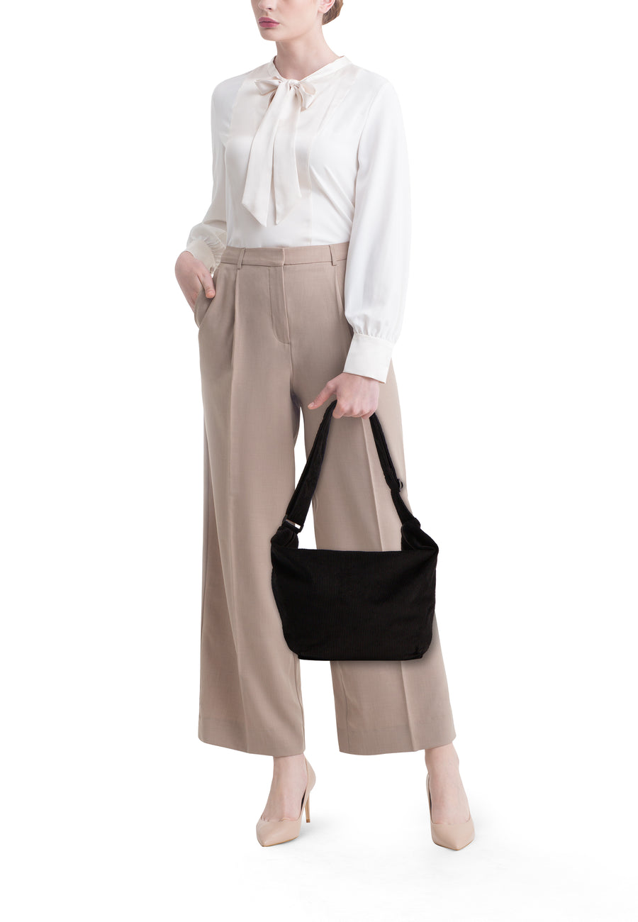Zwarte schoudertas van PIECES®, gedragen met een witte blouse en een beige broek.
