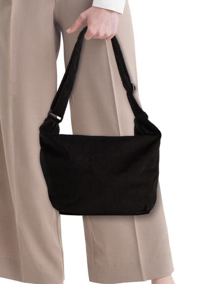 Zwarte ribfluwelen schoudertas van PIECES®, in de hand gedragen met een beige broek.