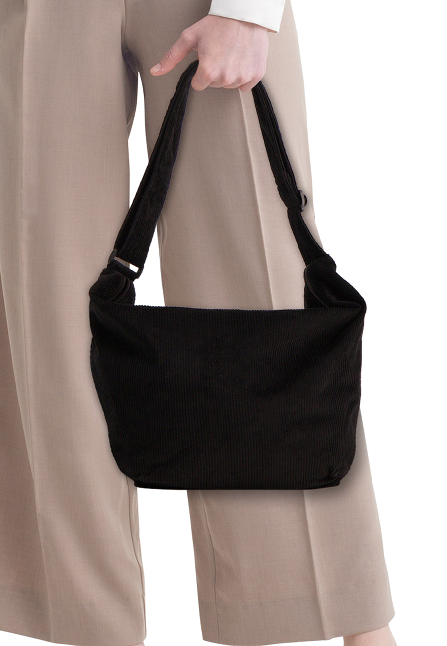 Zwarte ribfluwelen schoudertas van PIECES®, in de hand gedragen met een beige broek.