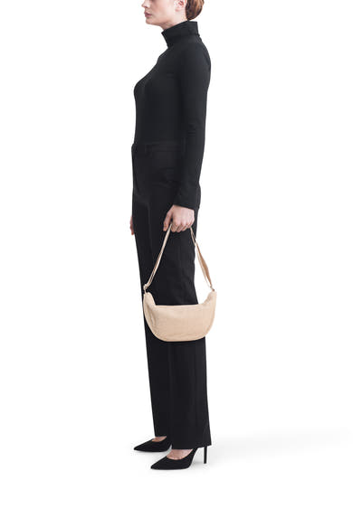 Sac à bandoulière beige en fausse fourrure de PIECES®, porté avec un pull à col roulé et un pantalon noirs.
