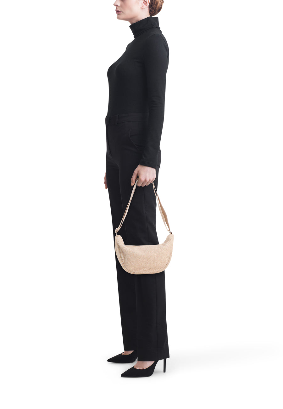 Sac à bandoulière beige en fausse fourrure de PIECES®, porté avec un pull à col roulé et un pantalon noirs.
