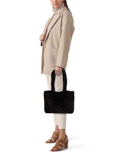 Sac à bandoulière noir du PIECES®, en fausse fourrure porté par une femme avec manteau beige.