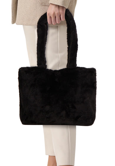 Sac à bandoulière noir en fausse fourrure de PIECES®, porté avec un manteau beige et un pantalon blanc.