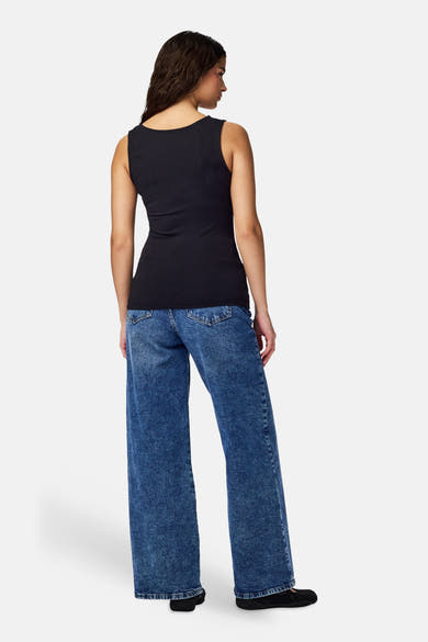 Zwart tanktop-achtig body van PIECES®, van achteren gedragen met een wijde blauwe spijkerbroek en zwarte platte schoenen.