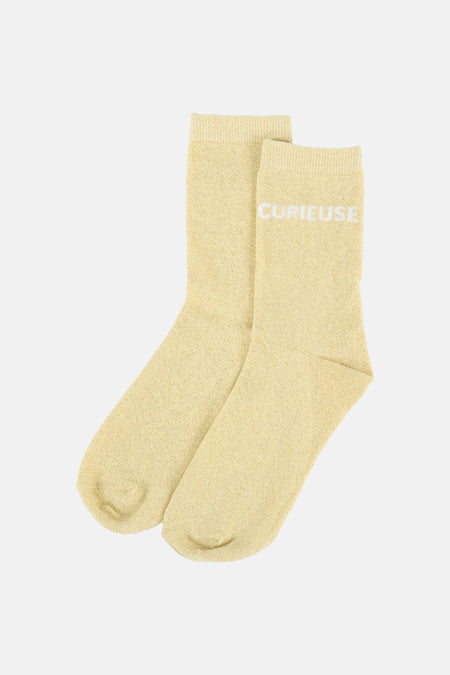 Gele glitter sokken van PIECES, gevouwen met de witte tekst "CURIEUSE".