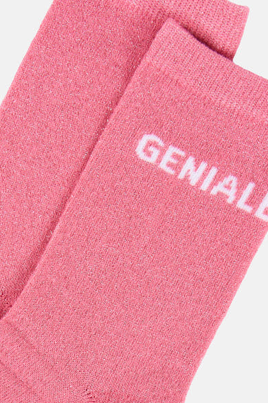Chaussettes roses pailletées de PIECES®, pliées avec le mot « GENIAL » imprimé en blanc.