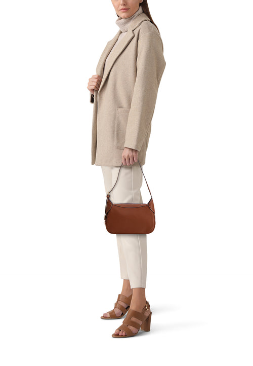 Bruine schoudertas van PIECES®, gedragen in de hand door een model, met een beige jas en bruine hakken.