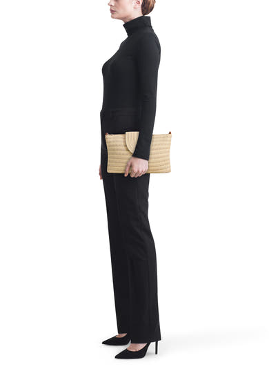 Beige schoudertas van PIECES®, van gevlochten stro, gedragen als clutch door een vrouw in het zwart, zijwaarts gezien.