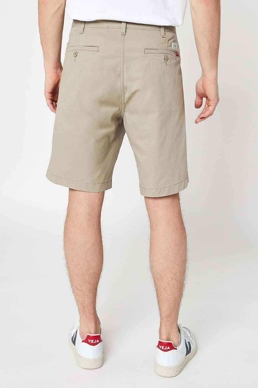 Short beige de Levi's, avec des poches arrière boutonnées et porté avec des chaussures blanches à rayures.