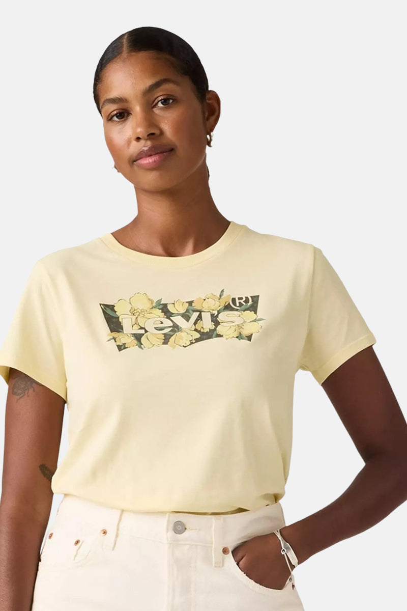 T-shirt jaune à manches courtes de Levi's, avec un logo floral et porté avec un jean blanc.