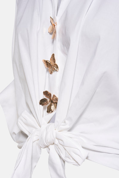 Chemisier blanc à manches courtes de Terra di Siena avec boutons décoratifs en forme de papillons dorés et noeud sur le devant.