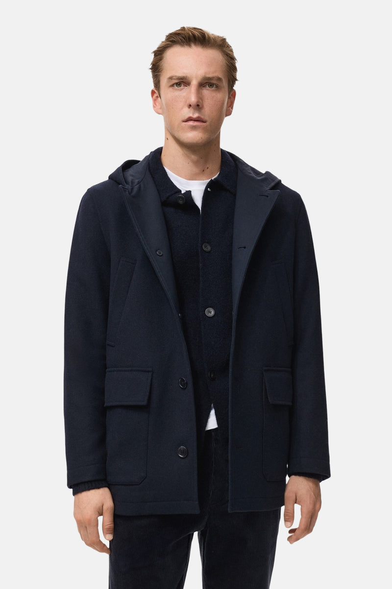Veste courte bleu foncé de MANGO, avec capuche et poches plaquées, portée sur une veste et un t-shirt blancs.