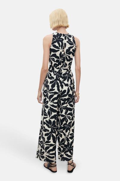 Zwarte bedrukte jumpsuit van MANGO, van achteren gezien, met een ritssluiting en zwarte sandalen.
