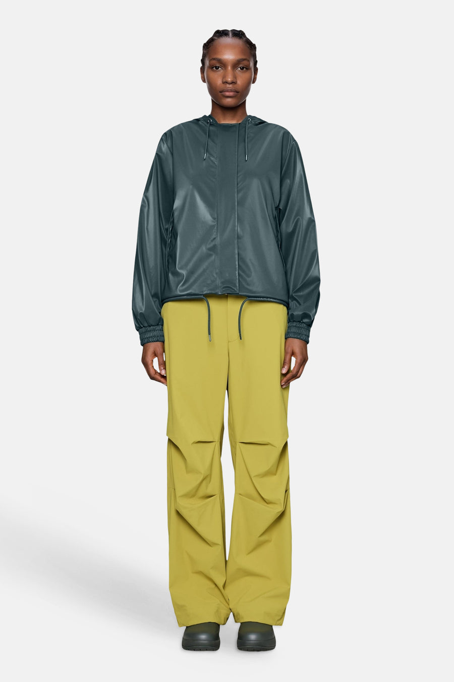 Dark green shiny casual jacket with hood and elastic cuffs, worn with mustard cargo pants and black shoes, front view