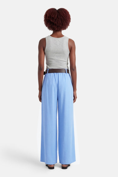 Pantalon de costume bleu de Terra di Siena, coupe ample et fluide, porté avec un débardeur gris et une ceinture marron.