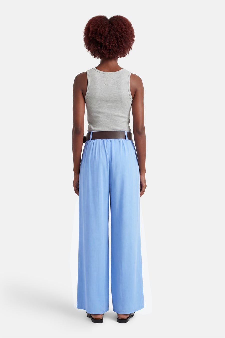 Pantalon de costume bleu de Terra di Siena, coupe ample et fluide, porté avec un débardeur gris et une ceinture marron.