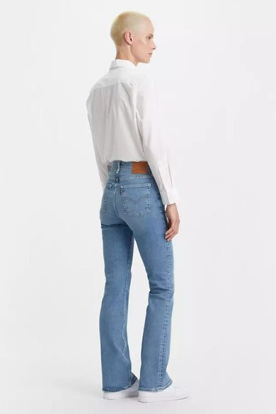 Jean bootcut bleu de Levi's, porté avec une chemise blanche boutonnée et des baskets blanches.