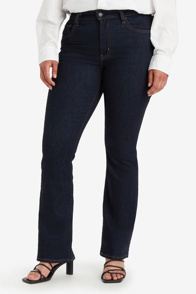 Bootcut jeans in donkerblauw denim van Levi's, gedragen met een wit overhemd en zwarte sandalen.