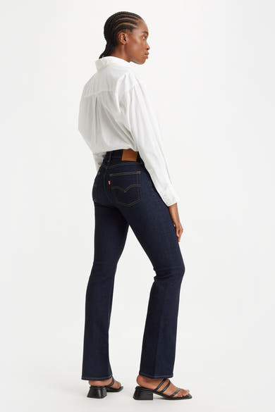 Jean bootcut en denim bleu foncé par Levi's, porté avec une chemise blanche et des sandales noires.