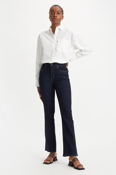 Donkerblauwe bootcut jeans van Levi's, gedragen met een wit overhemd en zwarte sandalen met hak.