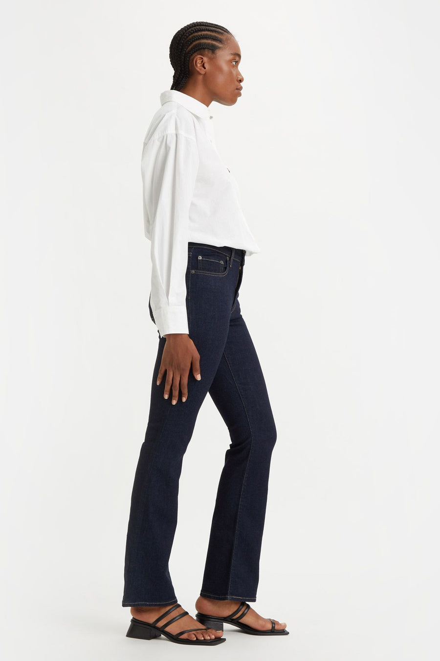 Donkerblauwe bootcut jeans van Levi's, gedragen met een wit overhemd en zwarte sandalen met hak, zijwaarts gezien.