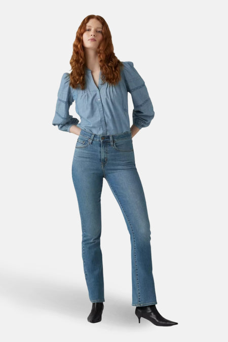 Jean bootcut en denim bleu moyen de Levi's, porté avec une chemise et des bottines noires.
