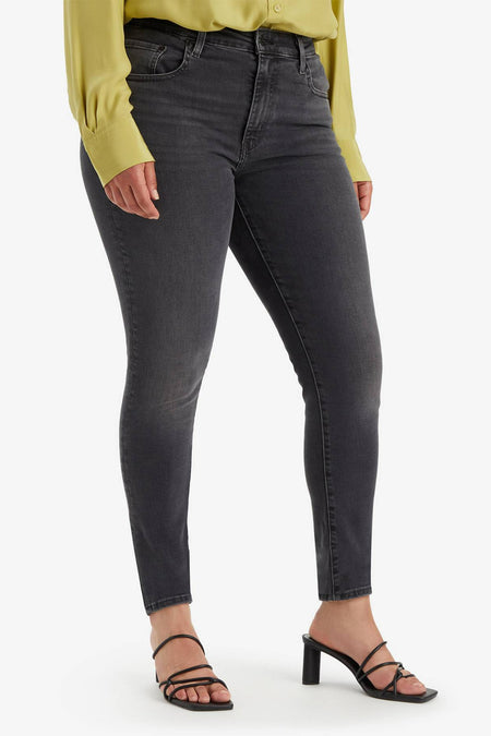 Jean skinny en denim gris foncé de Levi's, porté avec un chemisier jaune et des sandales à talons noirs.
