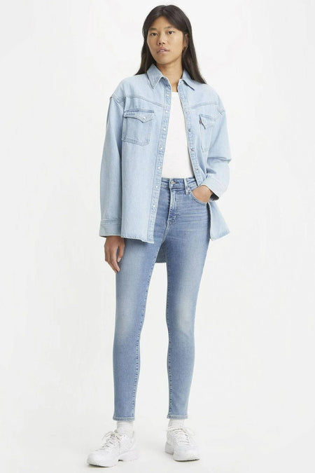 Jean skinny bleu clair de Levi's, porté avec une chemise en denim et des baskets blanches.