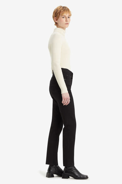 Jean droit en denim noir de Levi's, porté avec un pull à col roulé blanc et des bottines noires.