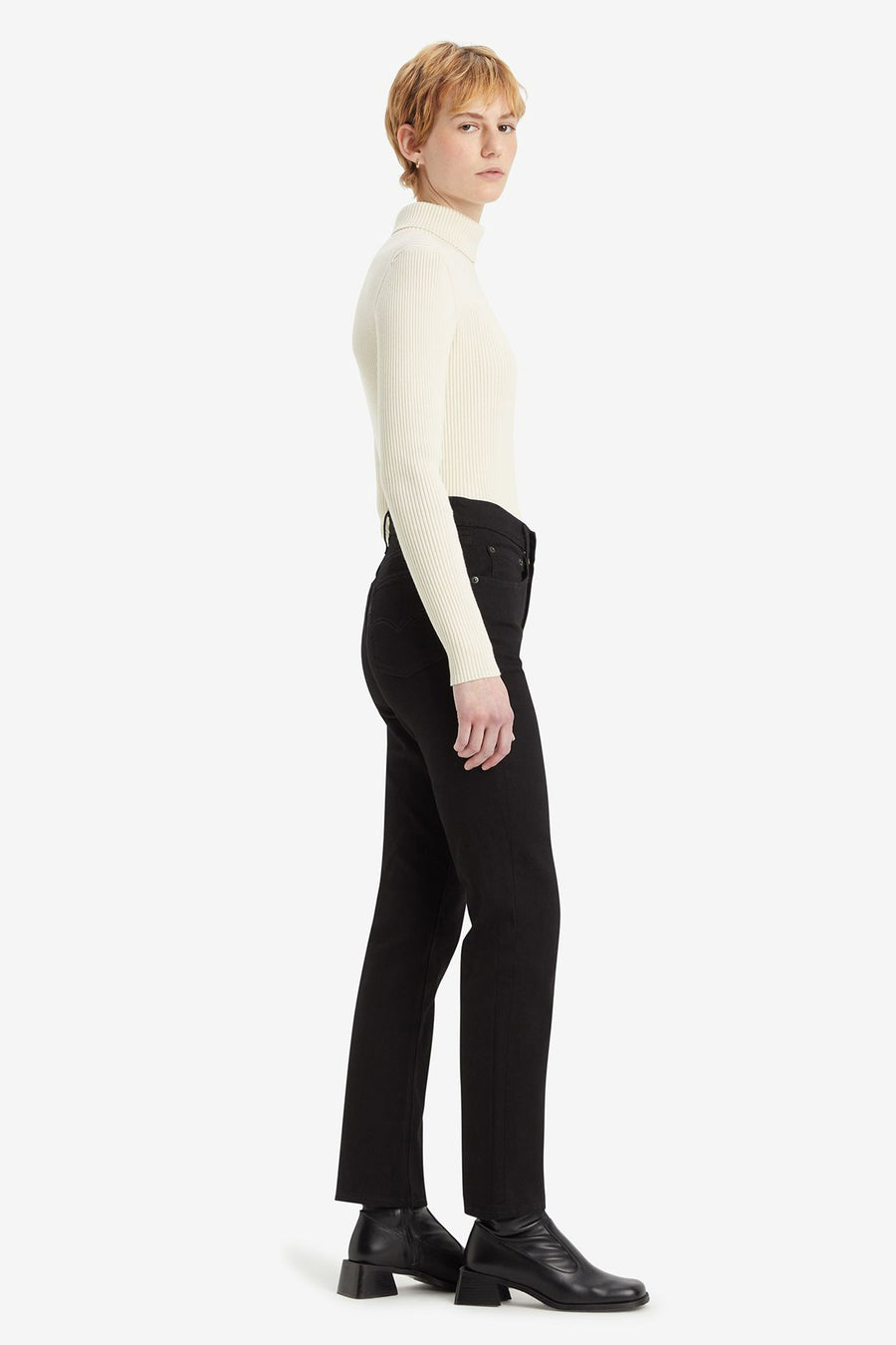 Jean droit en denim noir de Levi's, porté avec un pull à col roulé blanc et des bottines noires.