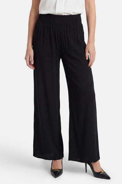 Black elastic waist wide-leg trousers with smocked waistband, worn with white top and black heels, front view